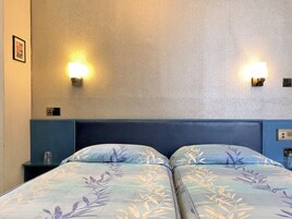 Ein Hotelzimmer mit zwei Betten, einem blauen Kopfteil und Wandleuchten.