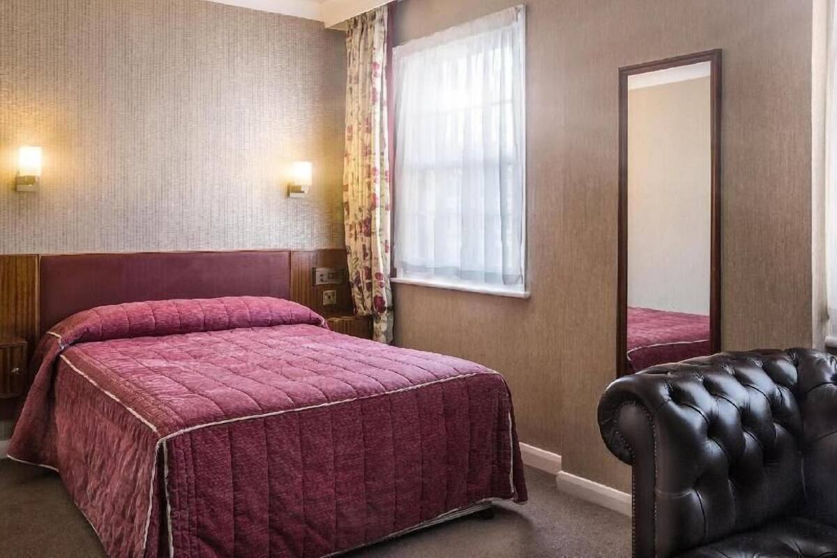 A hotel room with two beds, a large mirror, and a leather armchair.
