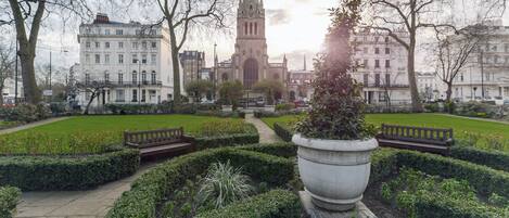 A historic building with a tall spire, surrounded by a well-manicured garden with benches and a pathway.