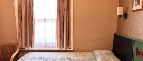 A hotel room with a bed, a chair, a desk, and a window with curtains.