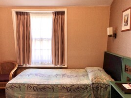 Ein Hotelzimmer mit Bett, Stuhl, Schreibtisch und einem Fenster mit Vorhängen.
