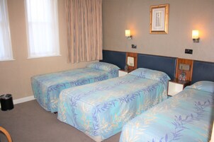 Une chambre d’hôtel avec deux lits simples, une petite poubelle, une table de chevet avec une lampe et un tableau encadré au mur.