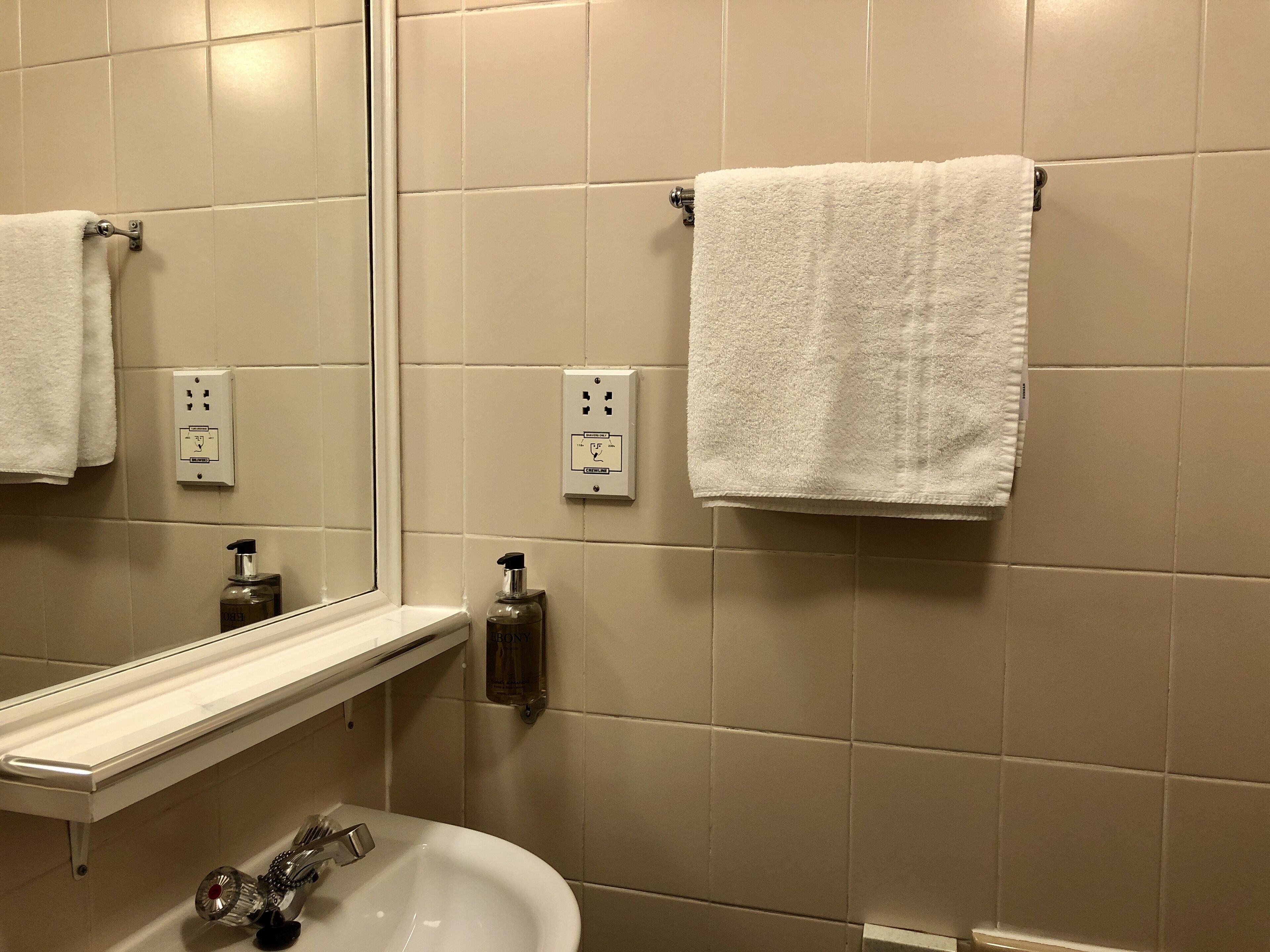 A bathroom with a white sink, a mirror, and two white towels hanging on the wall.