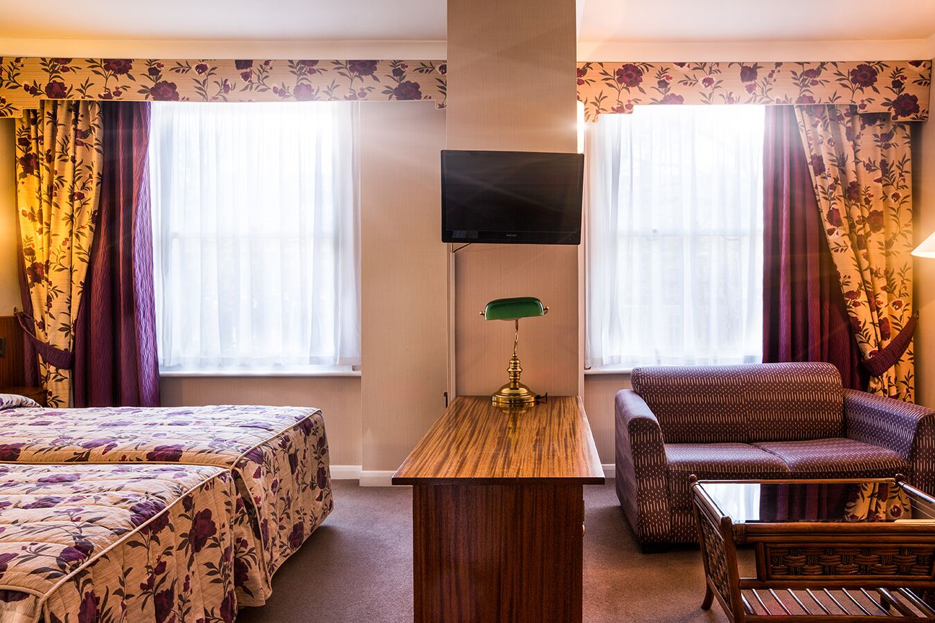 Et hotelværelse med en seng, en sofa, et fjernsyn og et skrivebord med en lampe.
