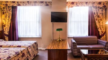 Una habitación de hotel con cama, sofá, televisión y escritorio con lámpara.