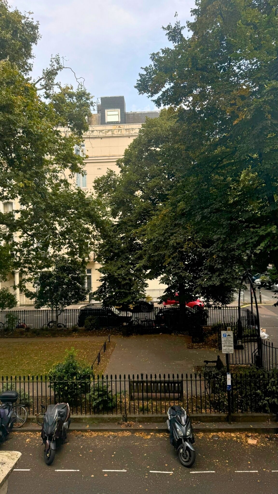 A street view with parked motorcycles, a fence, and trees.