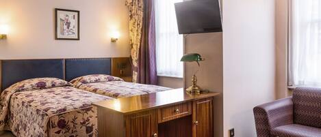 Habitación de hotel con cama, escritorio, silla, televisor y un cuadro en la pared.