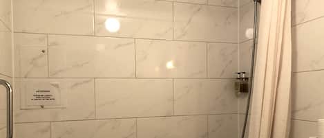 A bathroom with white marble tiles, a shower with a curtain, and a sign warning to be careful.