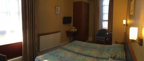 A hotel room with two beds, a chair, a desk, a television, and a wardrobe.