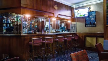 A bar area with wooden paneling, bar stools, and a counter displaying various bottles.