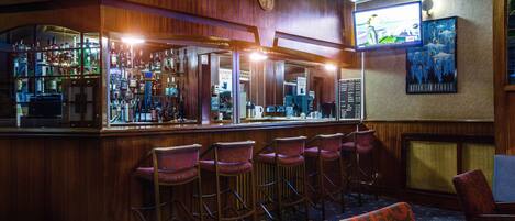 A bar area with wooden paneling, bar stools, and a counter displaying various bottles.