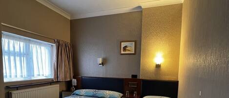Une chambre d’hôtel avec deux lits, une fenêtre avec des rideaux, un luminaire fixé au mur et un plafonnier.
