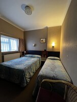 A hotel room with two beds, a window with curtains, a wall-mounted light, and a ceiling light fixture.