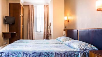 A hotel room with a bed, curtains, a television, a bedside table, and a wall-mounted light.