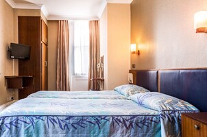 Ein Hotelzimmer mit Bett, Vorhängen, Fernseher, Nachttisch und Wandleuchte.