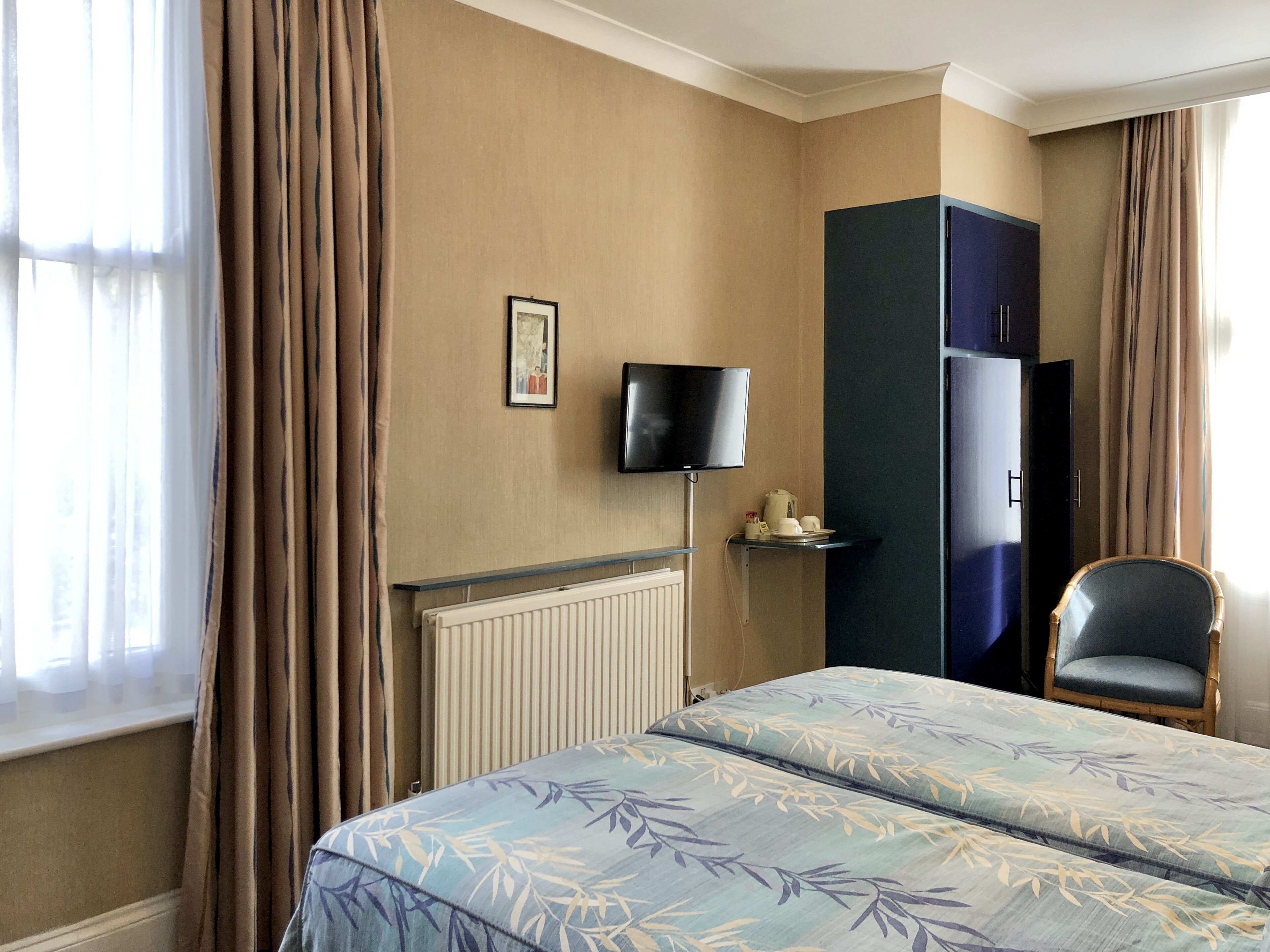 A hotel room with a bed, a TV mounted on the wall, a wardrobe, and a chair.