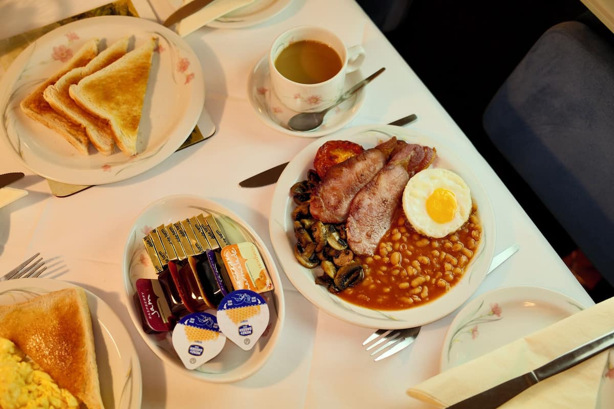 A breakfast setting with toast, eggs, beans, and bacon on plates, a cup of tea, and condiments.