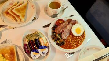 A breakfast setting with toast, eggs, beans, and bacon on plates, a cup of tea, and condiments.