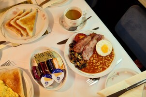 A breakfast setting with toast, eggs, beans, and bacon on plates, a cup of tea, and condiments.