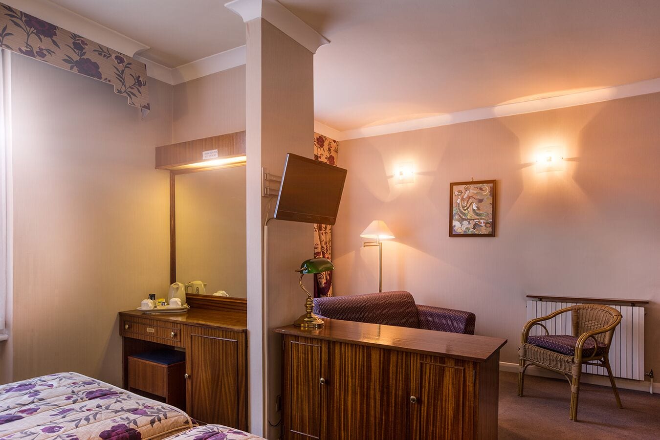 A hotel room with a bed, a wooden dresser, a chair, a desk, and a mirror.