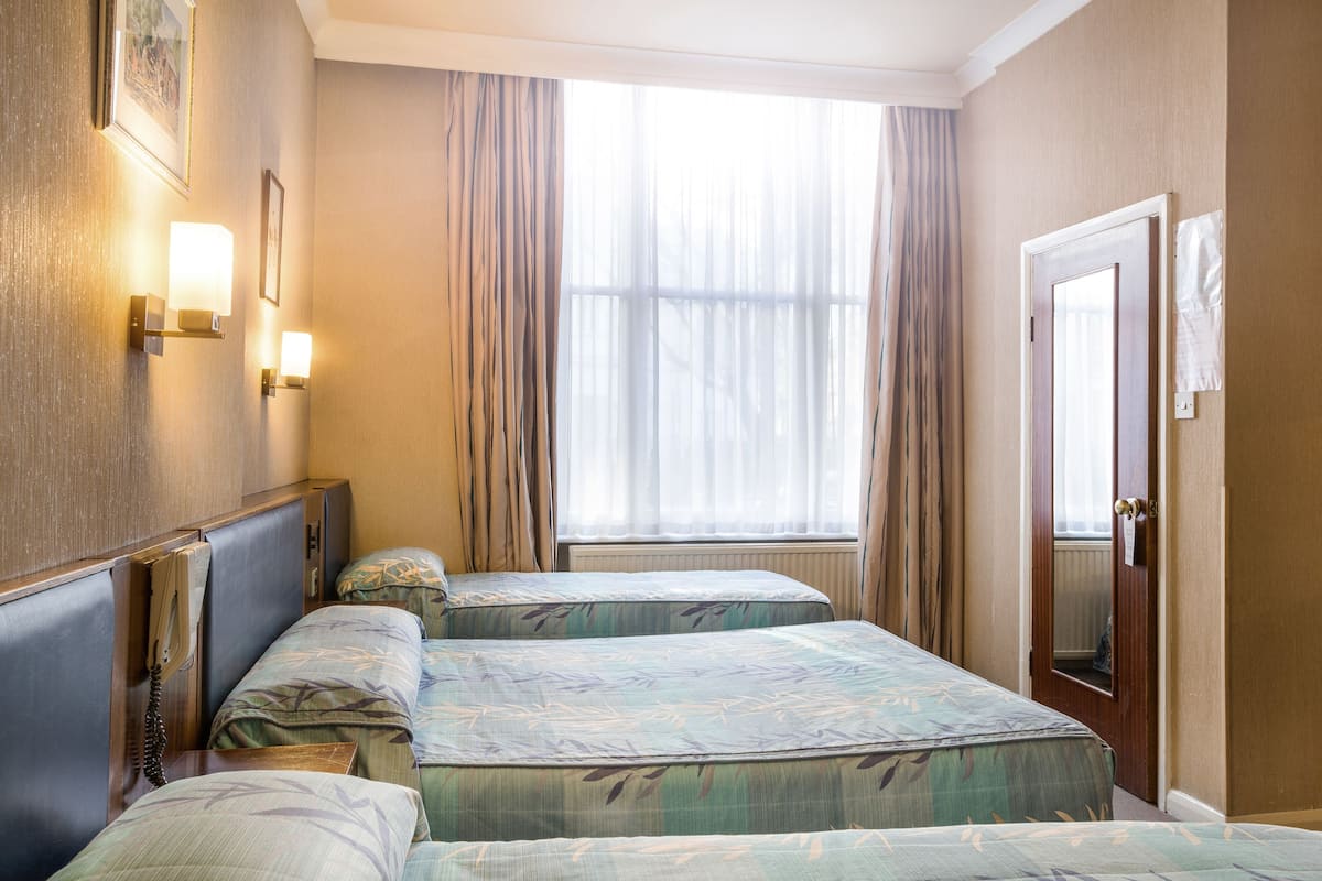 A hotel room with two beds, a window with curtains, a wall-mounted phone, and a door with a towel hanging on it.