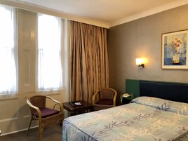 Ein Hotelzimmer mit einem Bett, zwei Sessel, einem kleinen Tisch, einem Nachttisch, einer Lampe und einem Bild an der Wand.