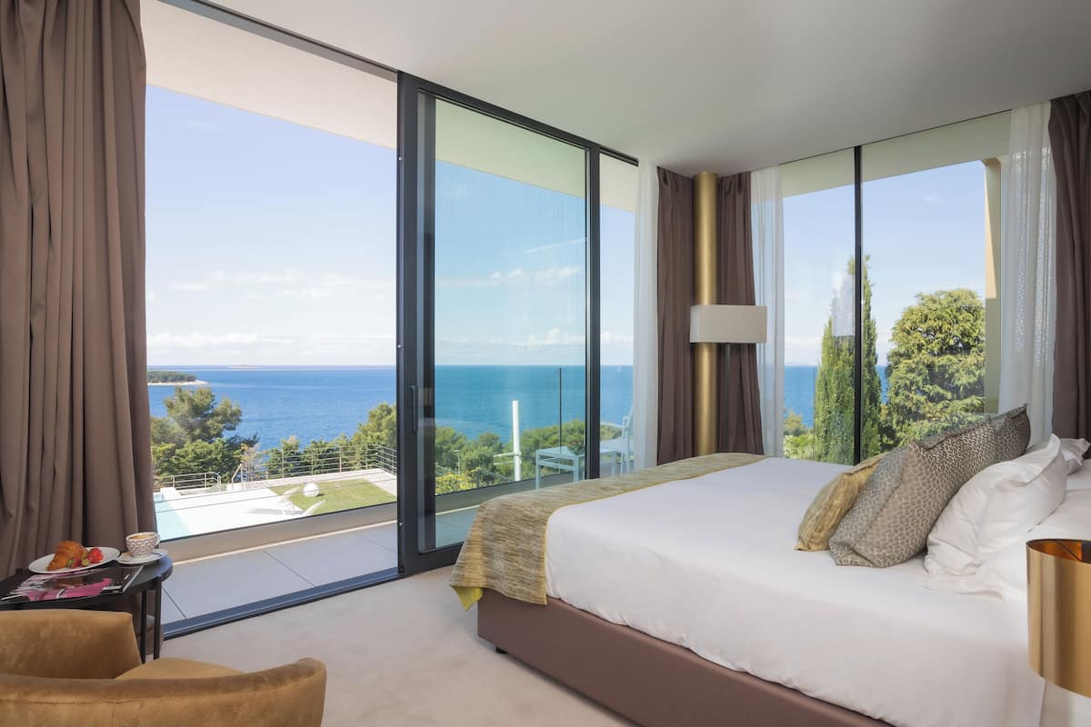 A bedroom with a large bed, a view of the sea, and a balcony with a table and chair.