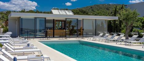 A modern poolside area with lounge chairs, a pool, and a building with large windows.