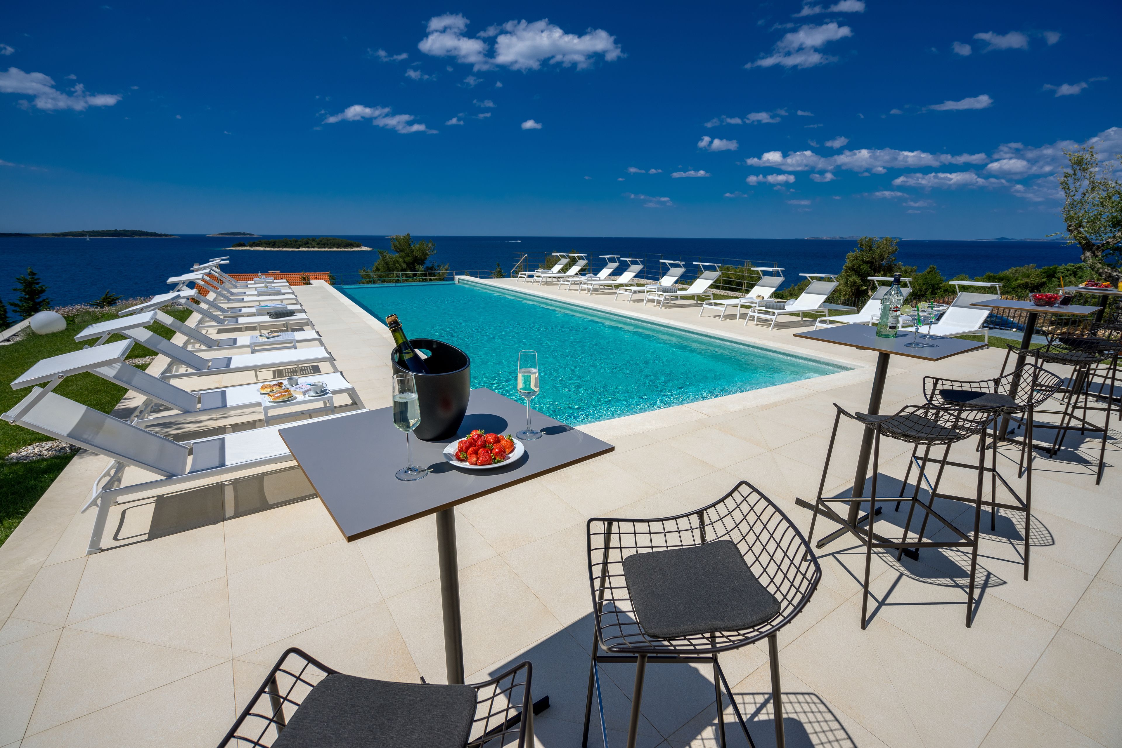 Ein Poolbereich mit Liegestühlen, einem Tisch mit einer Champagnerflasche und Blick aufs Meer.