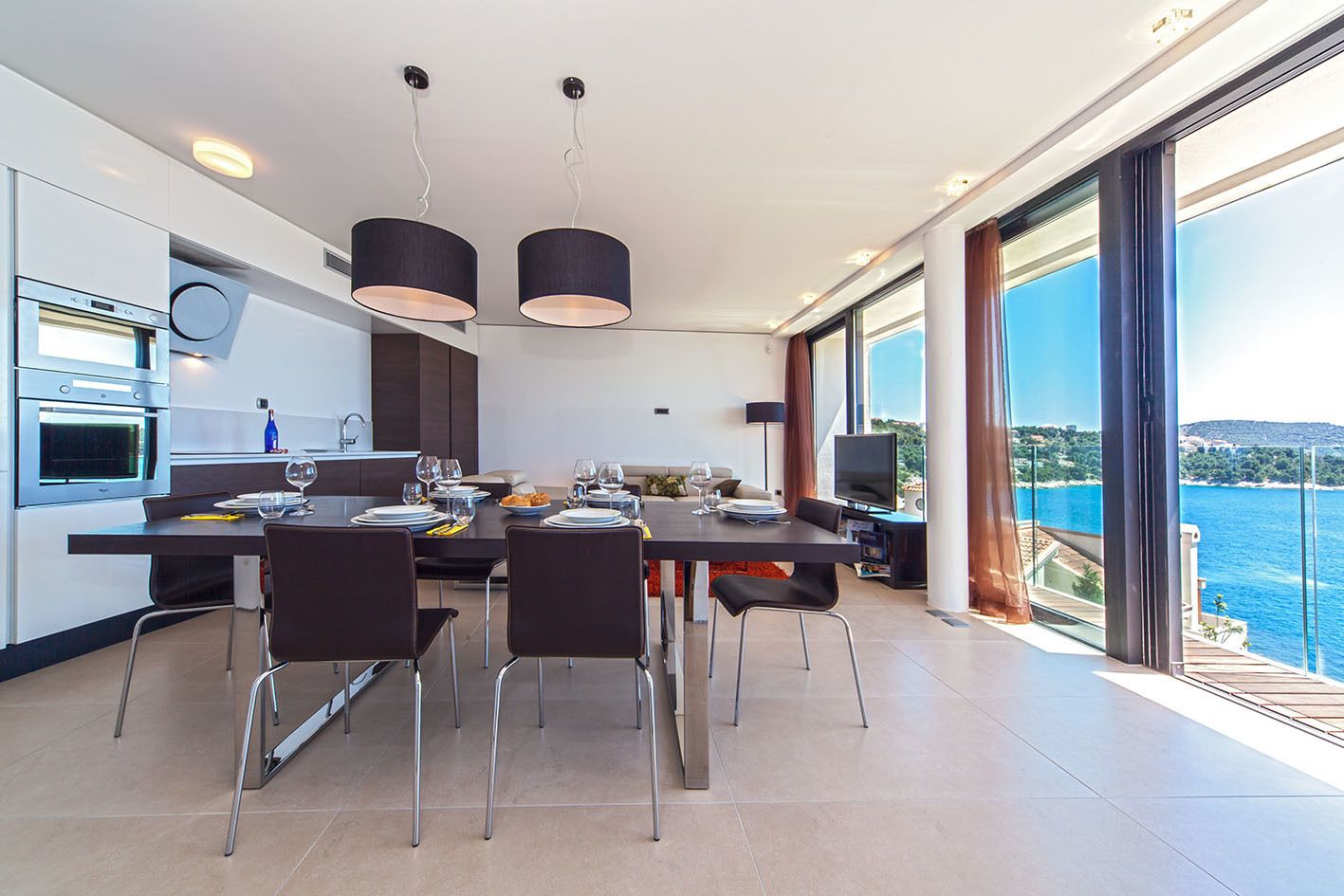 Cozinha moderna com eletrodomésticos embutidos, espaço de jantar com vista para o mar e televisão de tela plana.