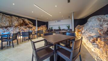 A modern dining area with a large table and chairs, a rock wall, and a ceiling with recessed lighting.