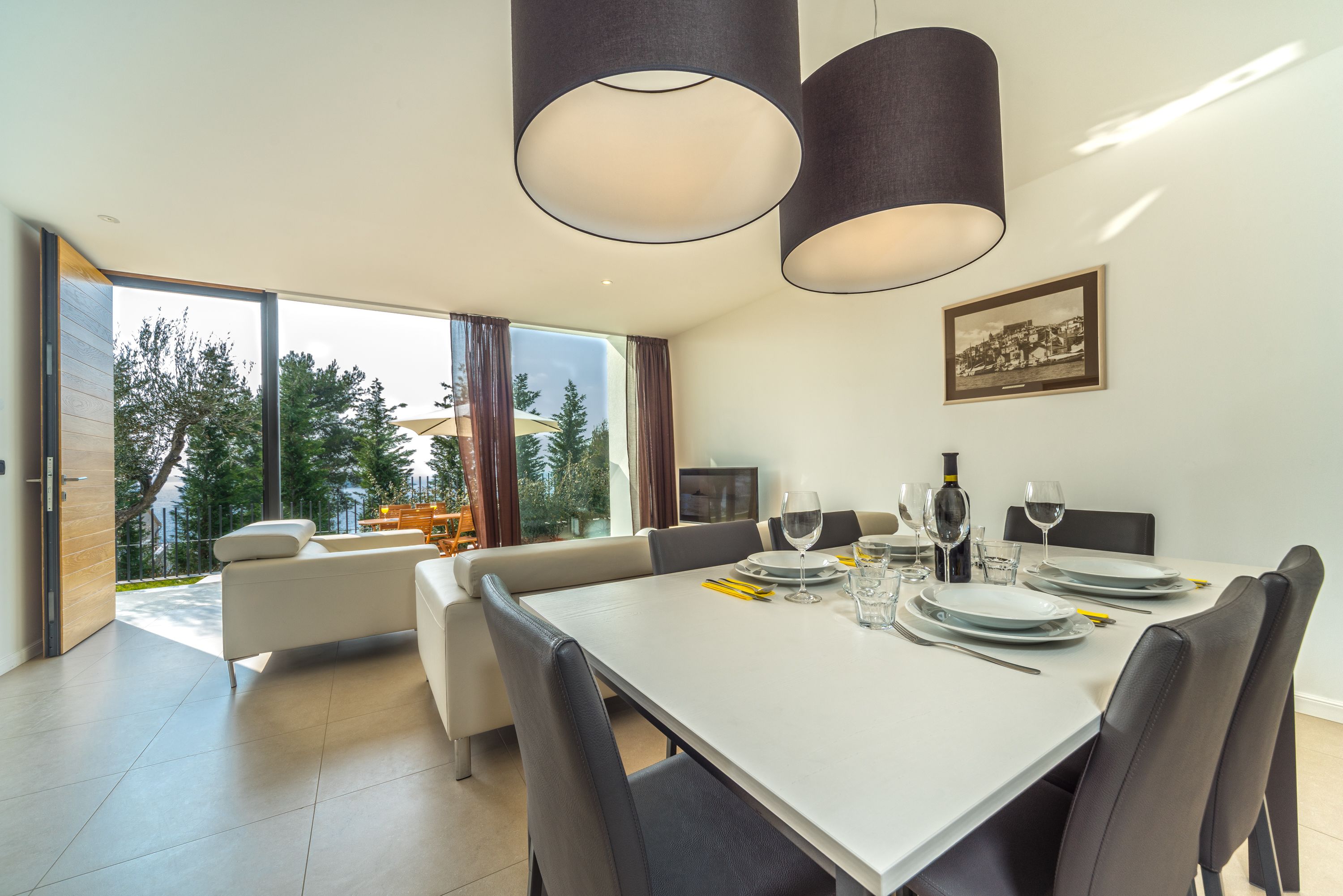 Un comedor moderno con una mesa blanca para seis, sillas negras y un amplio ventanal con vistas a árboles y un edificio.