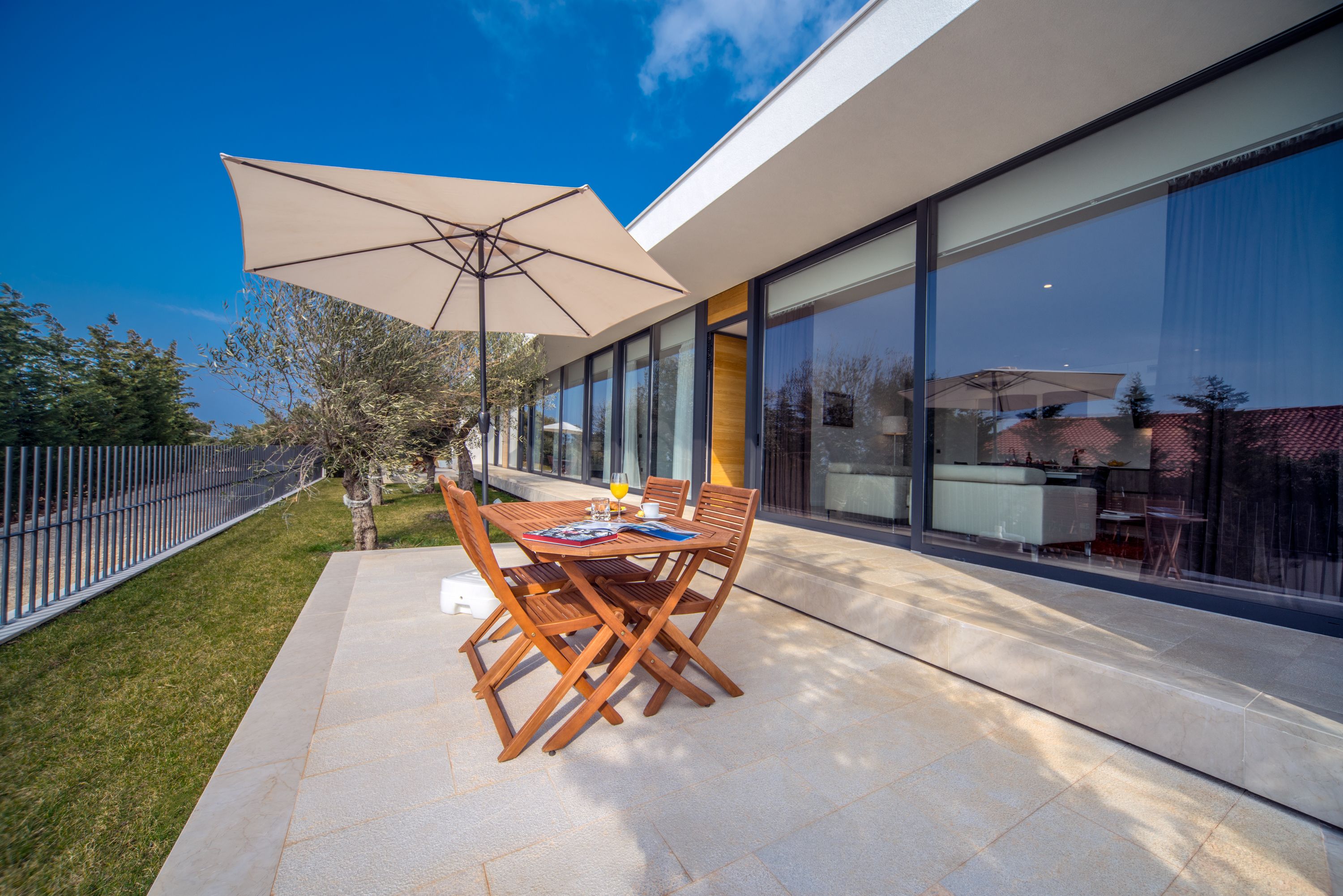 A modern outdoor patio with a table and chairs, a large umbrella, and a glass building in the background.