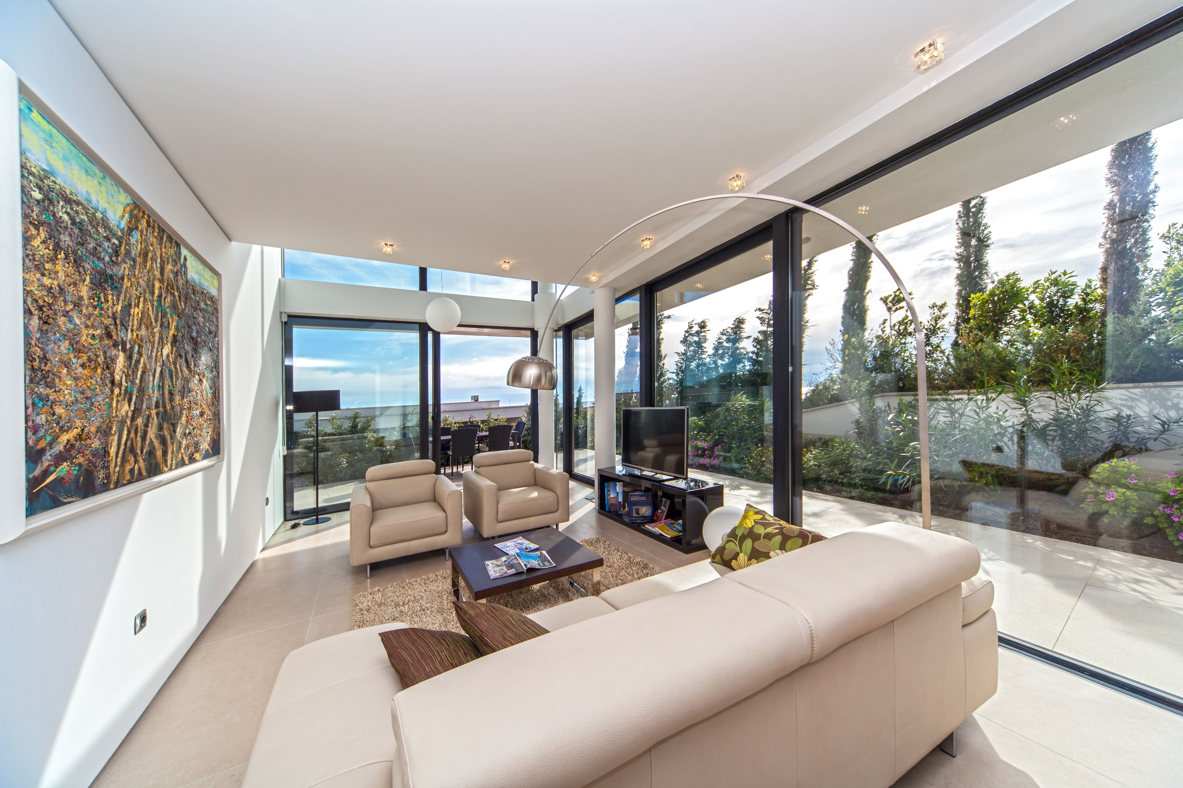 Una sala de estar moderna con un sofá grande, sillones, una mesa de centro y un televisor. Una ventana amplia ofrece vistas a árboles y un jardín.