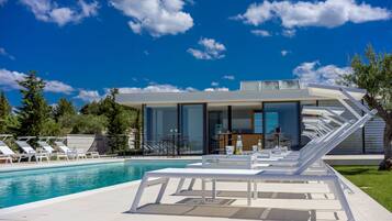 A modern poolside area with lounge chairs, a pool, and a contemporary building with large windows.