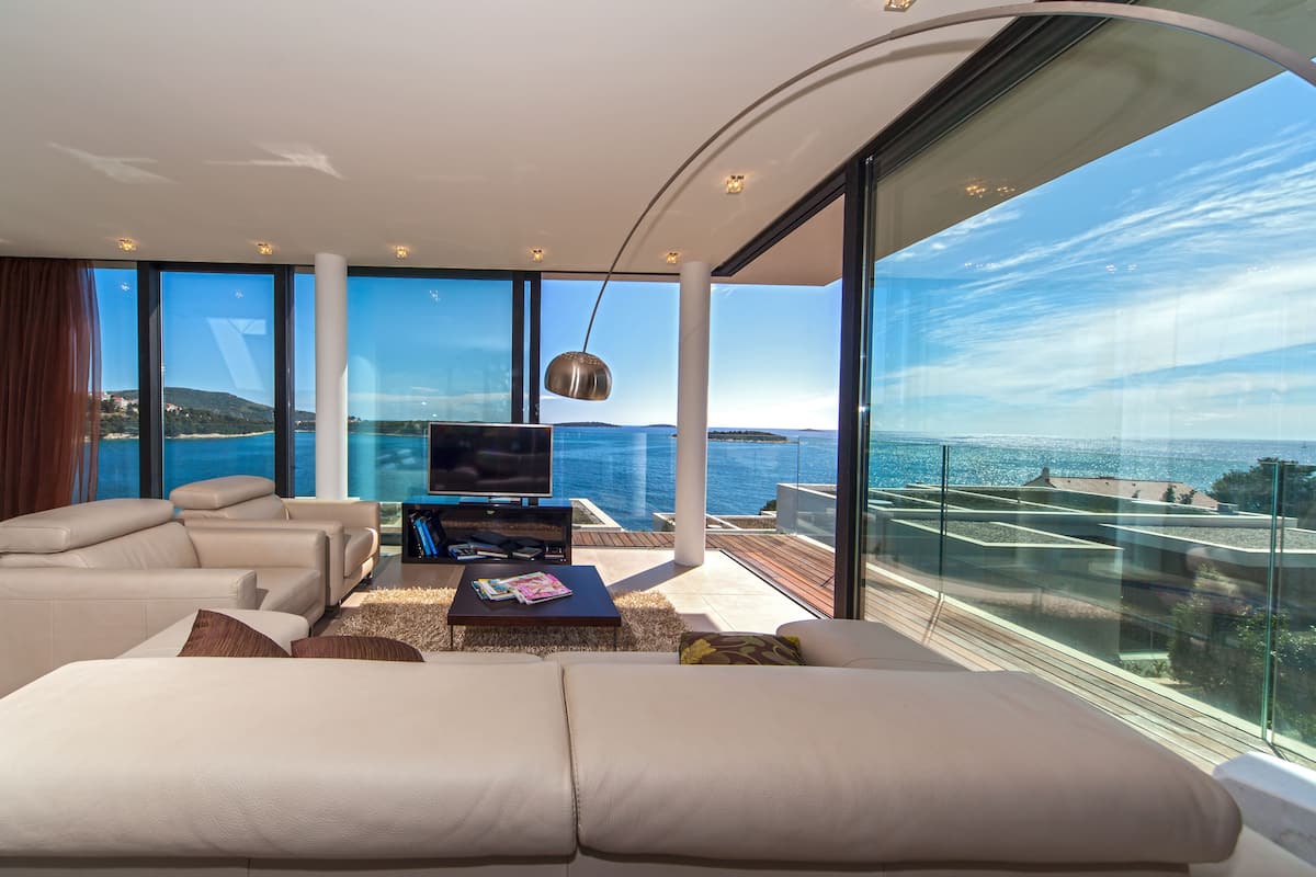 A modern living room with a large TV, comfortable seating, and a view of the sea.