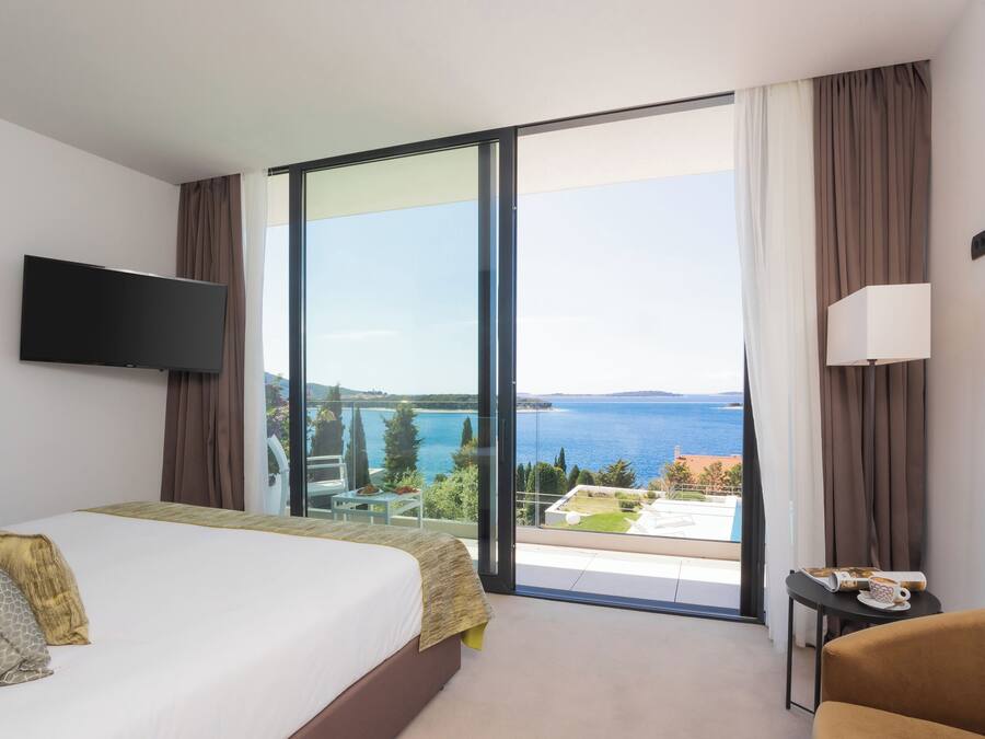 A hotel room with a bed, a television, a table with a lamp, and a view of the sea.