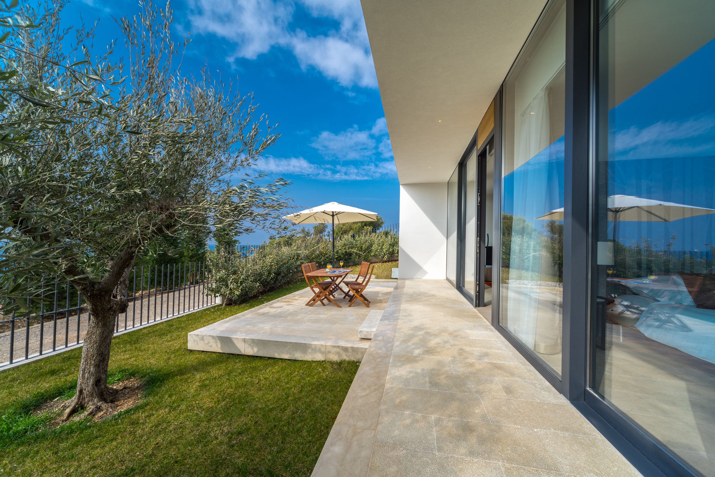 A modern outdoor patio with a table and chairs, a tree, and a glass building facade.