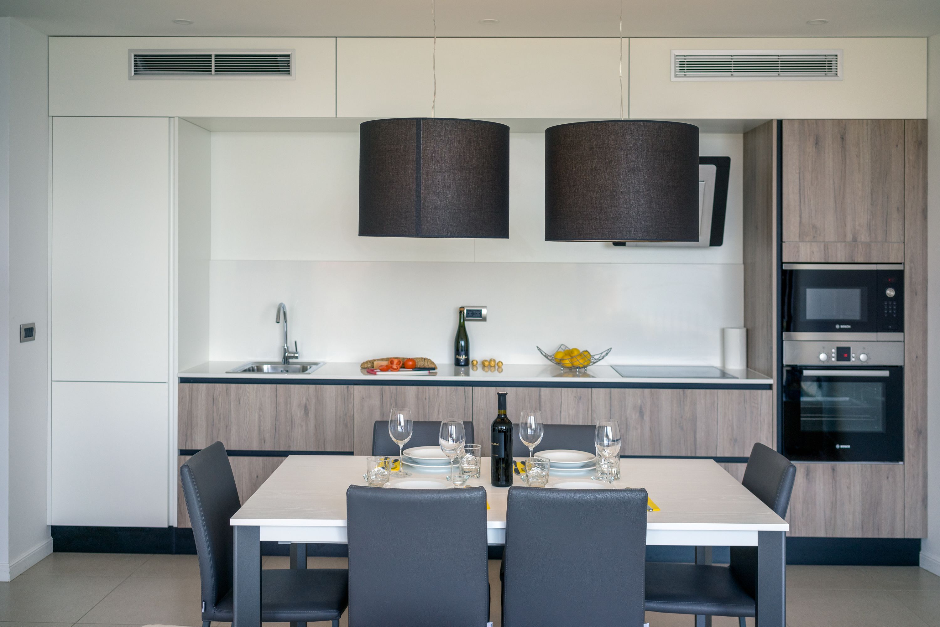 Una cocina moderna con comedor, que incluye una mesa blanca para dos, un microondas y un horno empotrado.