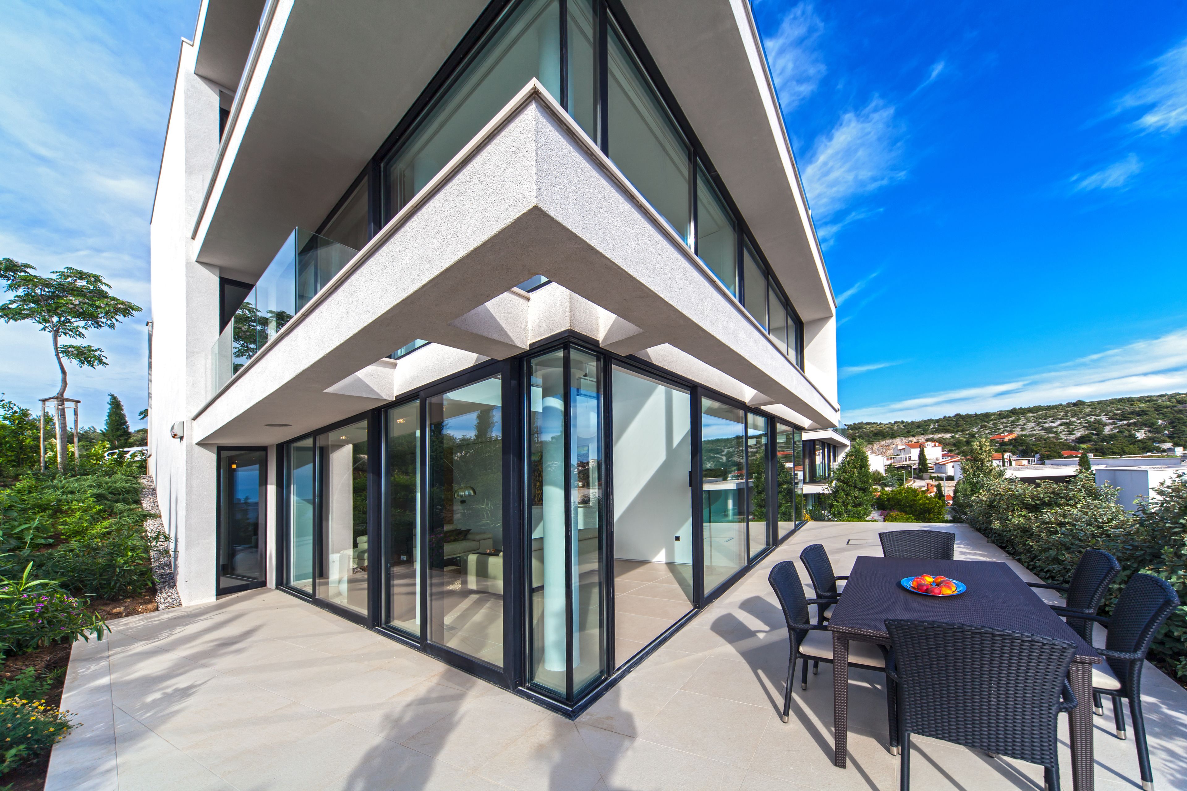 A modern house with a glass facade, outdoor seating, and a view of the surrounding area.