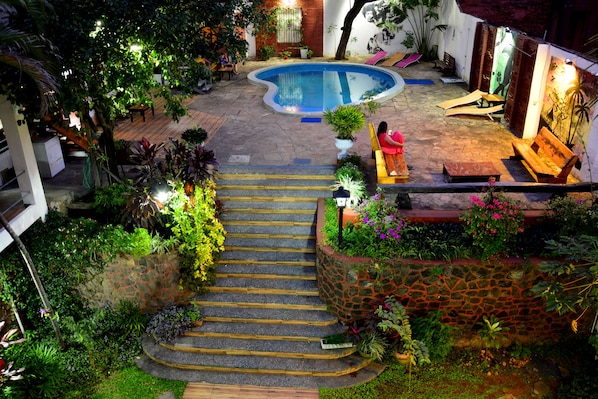 A pool area with steps leading down to a lower level, surrounded by lush greenery and outdoor seating. - El Viajero Asuncion Hostel & Suites (Asunción)