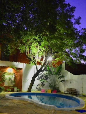 A swimming pool with a mural, surrounded by trees and a bench. - El Viajero Asuncion Hostel & Suites (Asunción)