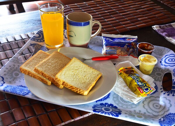 A plate with two slices of toast, a glass of orange juice, a mug, a packet of butter, and a packet of sugar. - El Viajero Asuncion Hostel & Suites (Asunción)