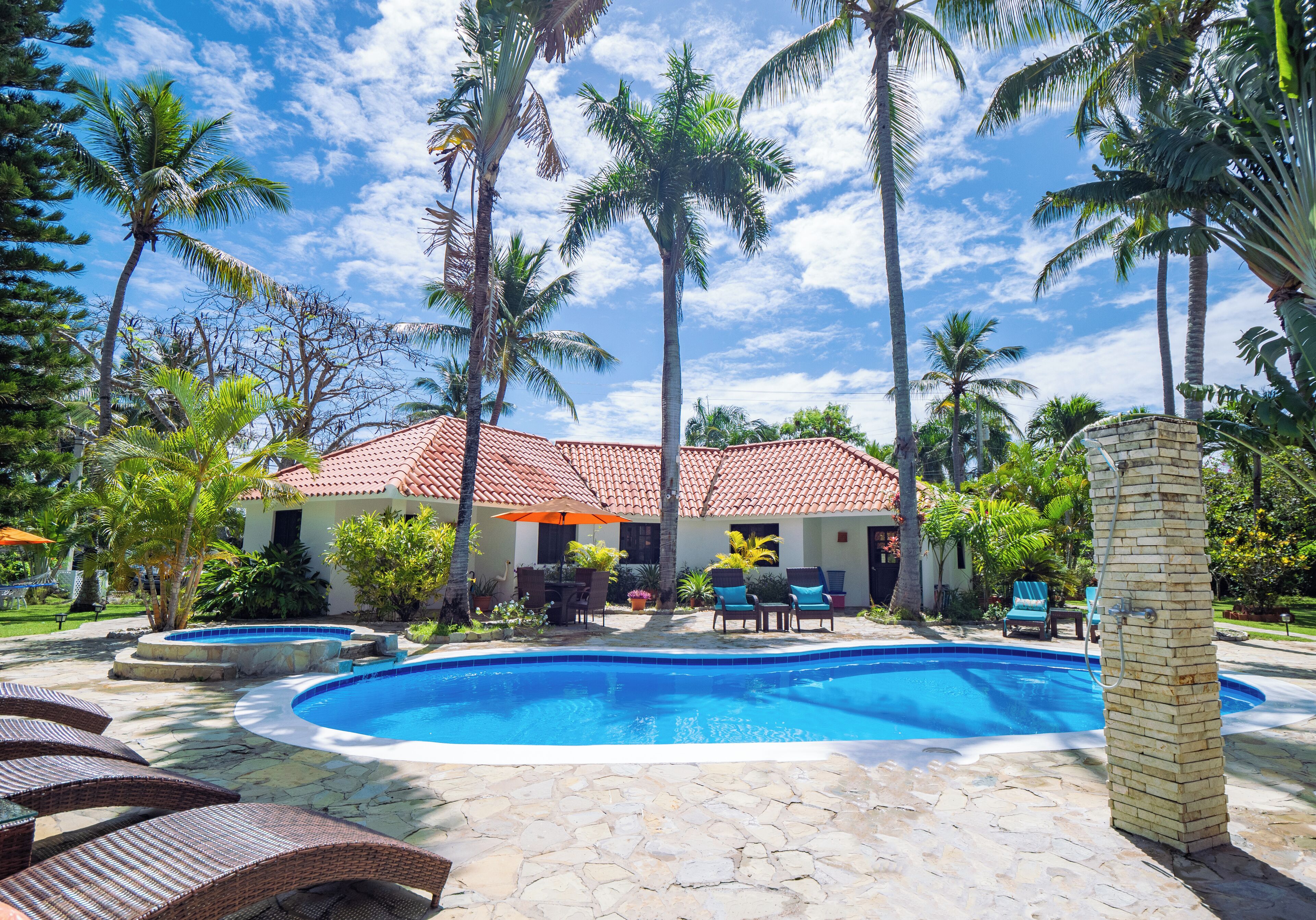 A swimming pool with lounge chairs and a house with a red-tiled roof.