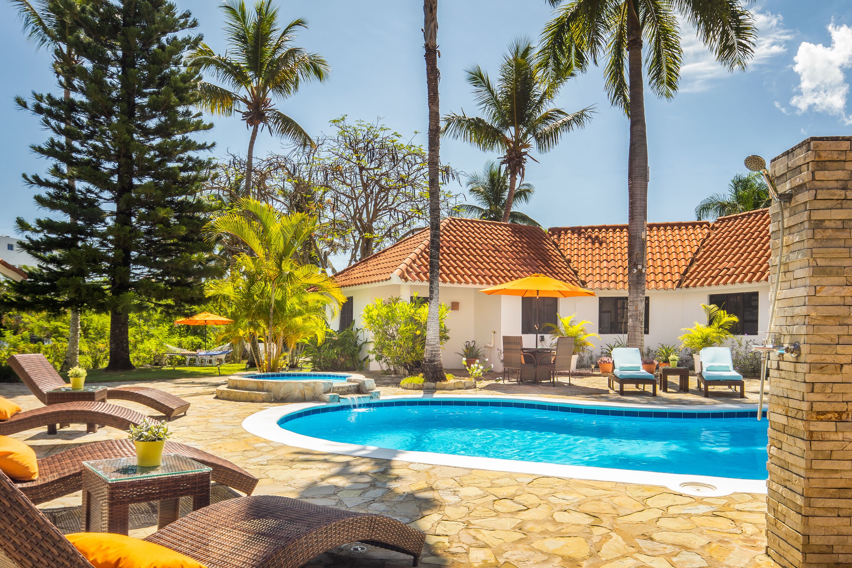 A swimming pool with lounge chairs, palm trees, and a tiled-roof building.