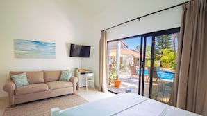 A hotel room with a bed, a sofa, a TV, a desk, and a view of an outdoor pool area.
