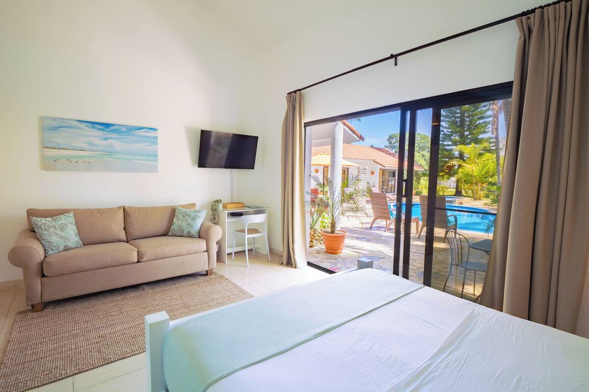 Une chambre d’hôtel comprenant un lit, un canapé, une télévision, un bureau et donnant sur une piscine extérieure.