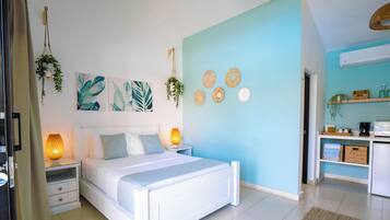 Un dormitorio con cama, mesitas de noche, aire acondicionado instalado en la pared y una zona de kitchenette.
