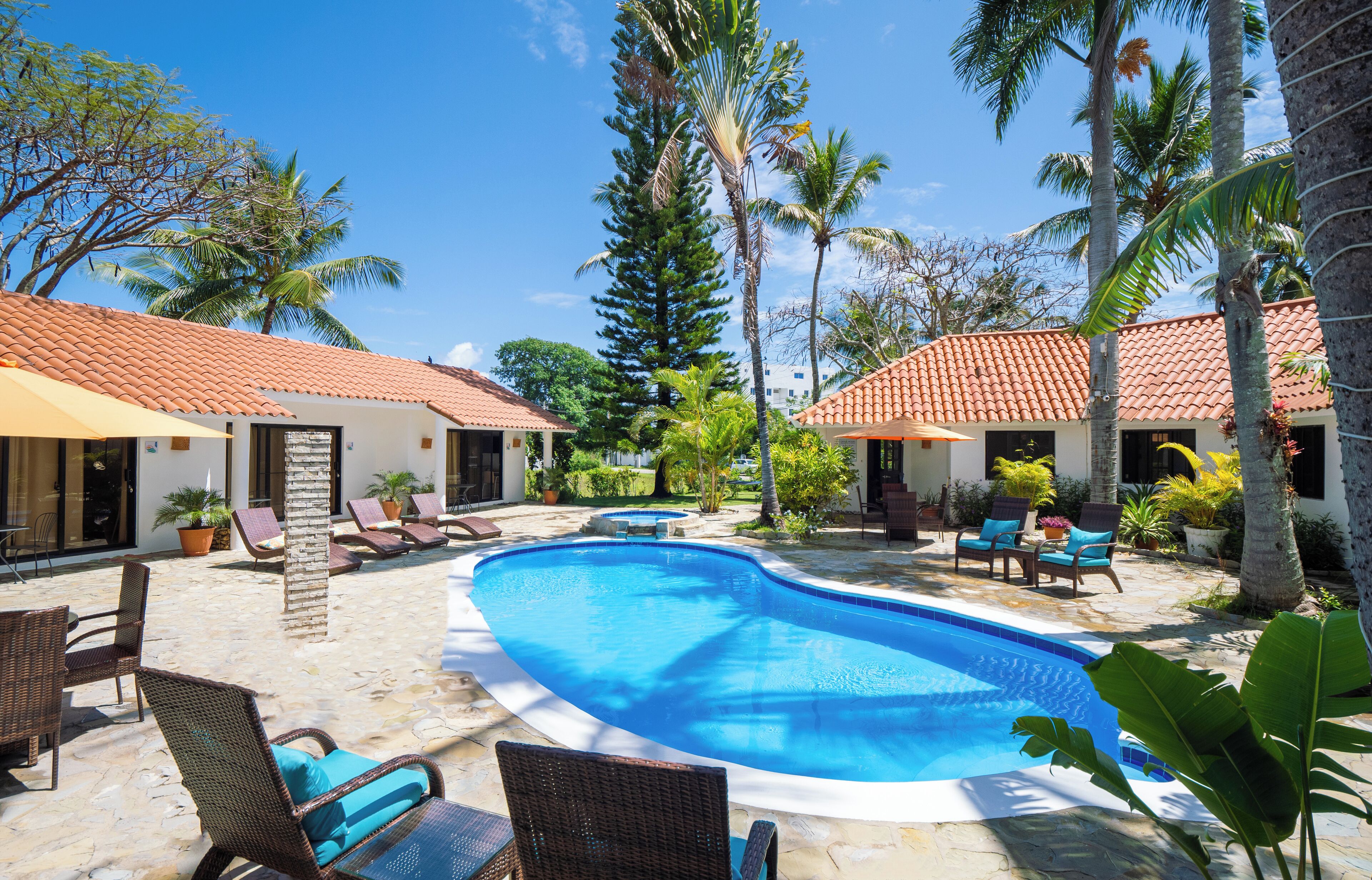 A swimming pool with lounge chairs and palm trees, surrounded by buildings with red-tiled roofs.