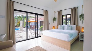 A bedroom with a large bed, sliding glass doors to an outdoor area, a ceiling fan, and a small table with a lamp.